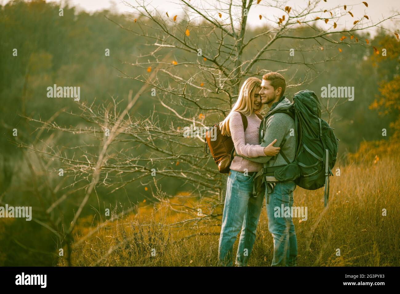 Couple heureux admire de la nature debout avec des sacs à dos sur l'herbe d'automne. Un jeune homme et une jeune femme caucasiens sourit embrasser tout en enjo Banque D'Images