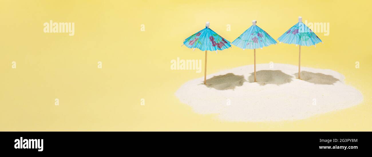 Île de sable avec trois parasols bleus sur fond jaune en plein soleil, concept de vacances d'été à la plage, bannière, gros plan. Banque D'Images