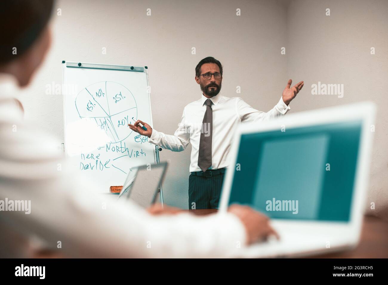 Le chef présente un plan d'affaires à ses collègues. Homme dans une chemise blanche avec une cravate se tient sur le tableau avec un schéma. BT bureau Banque D'Images