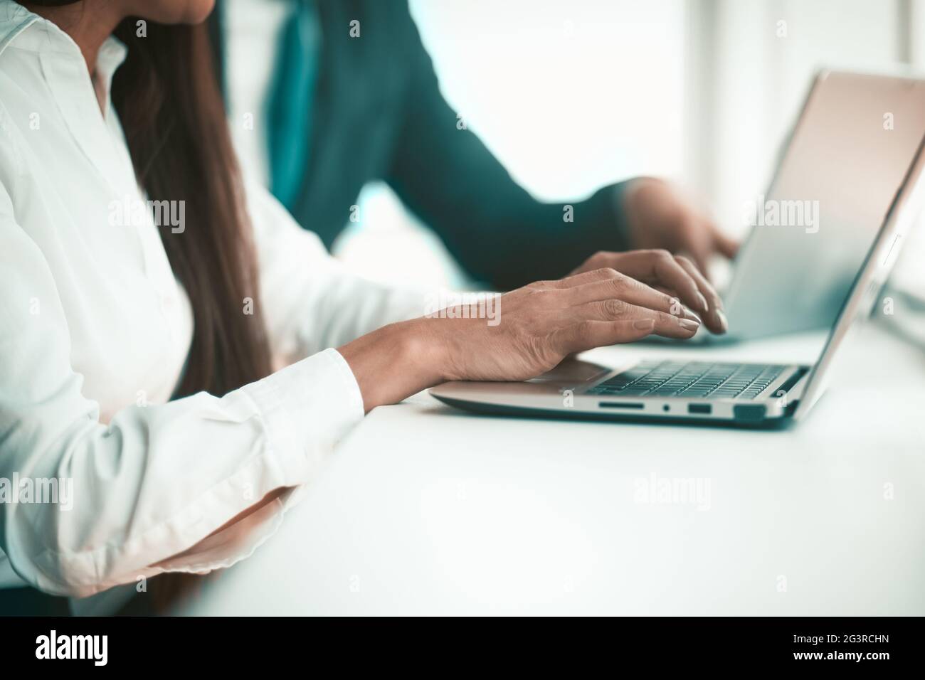 Les employés de bureau à un ordinateur portable. Les mains de l'employé sont imprimées sur le clavier. En arrière-plan se trouve un collègue dans un costume. Quali élevé Banque D'Images