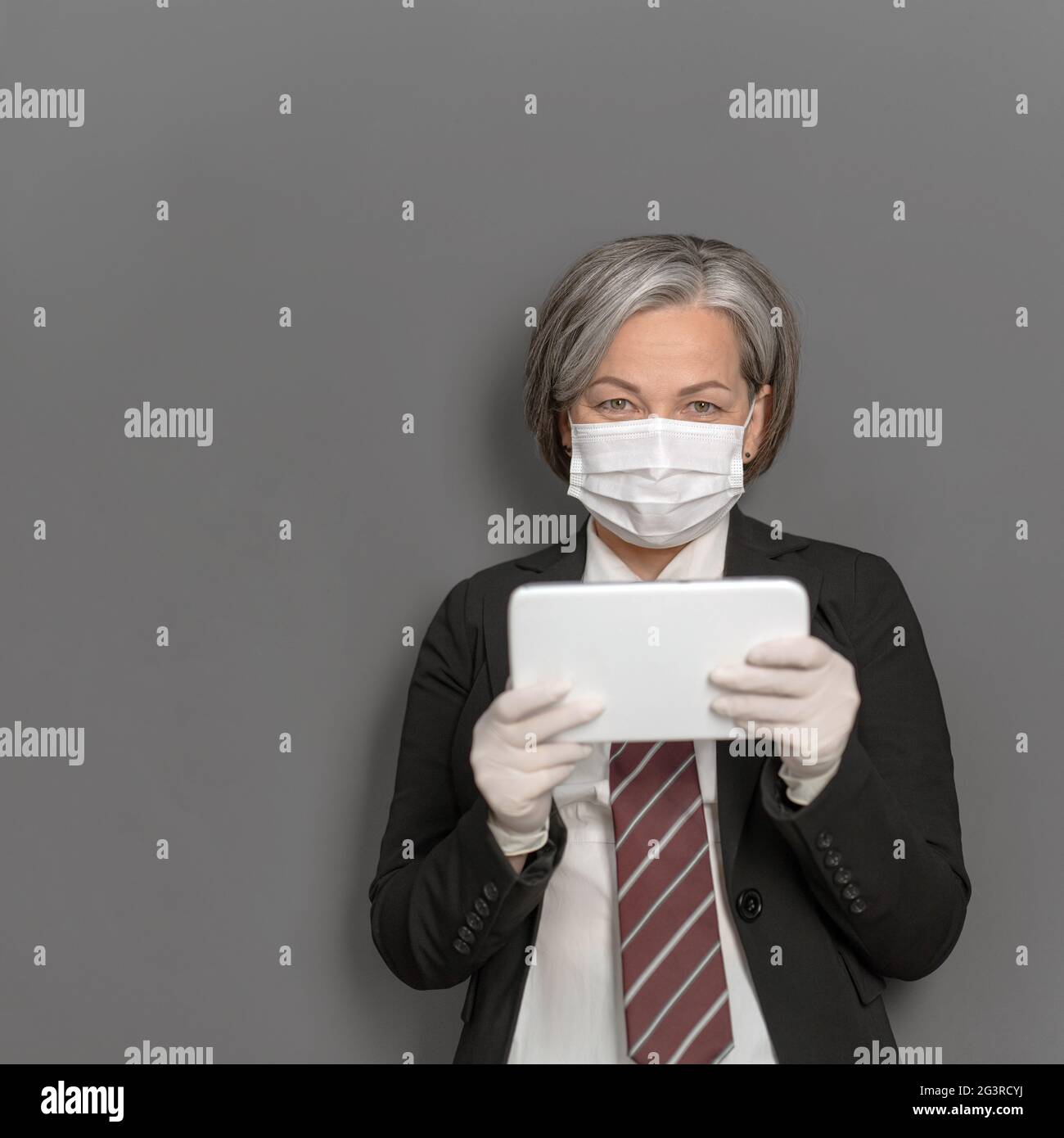 Femme d'affaires caucasienne dans le masque de protection travaille le gadget numérique. Une femme grise regarde la caméra qui tient la tablette avant elle Banque D'Images
