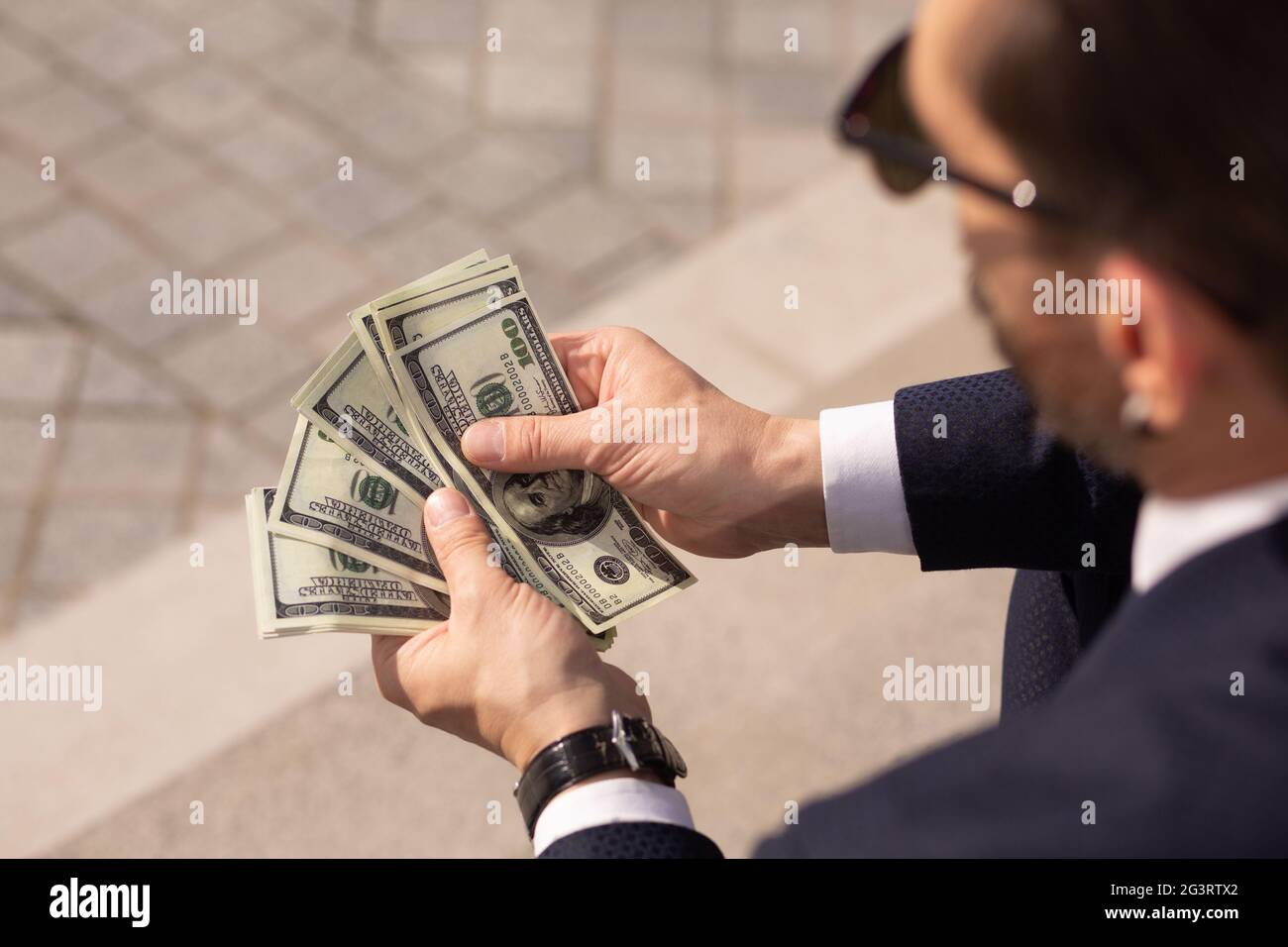 Gros plan sur un homme d'affaires américain prospère qui songe à une Wad de billets de 100 dollars tout en étant assis sur le trottoir. Vue arrière Banque D'Images