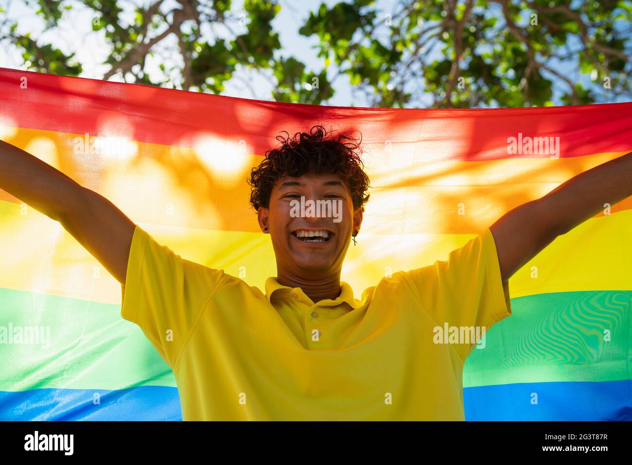 Le jeune homme gay tient fièrement le drapeau lgbt entre ses mains devant la mer, inclusive Banque D'Images