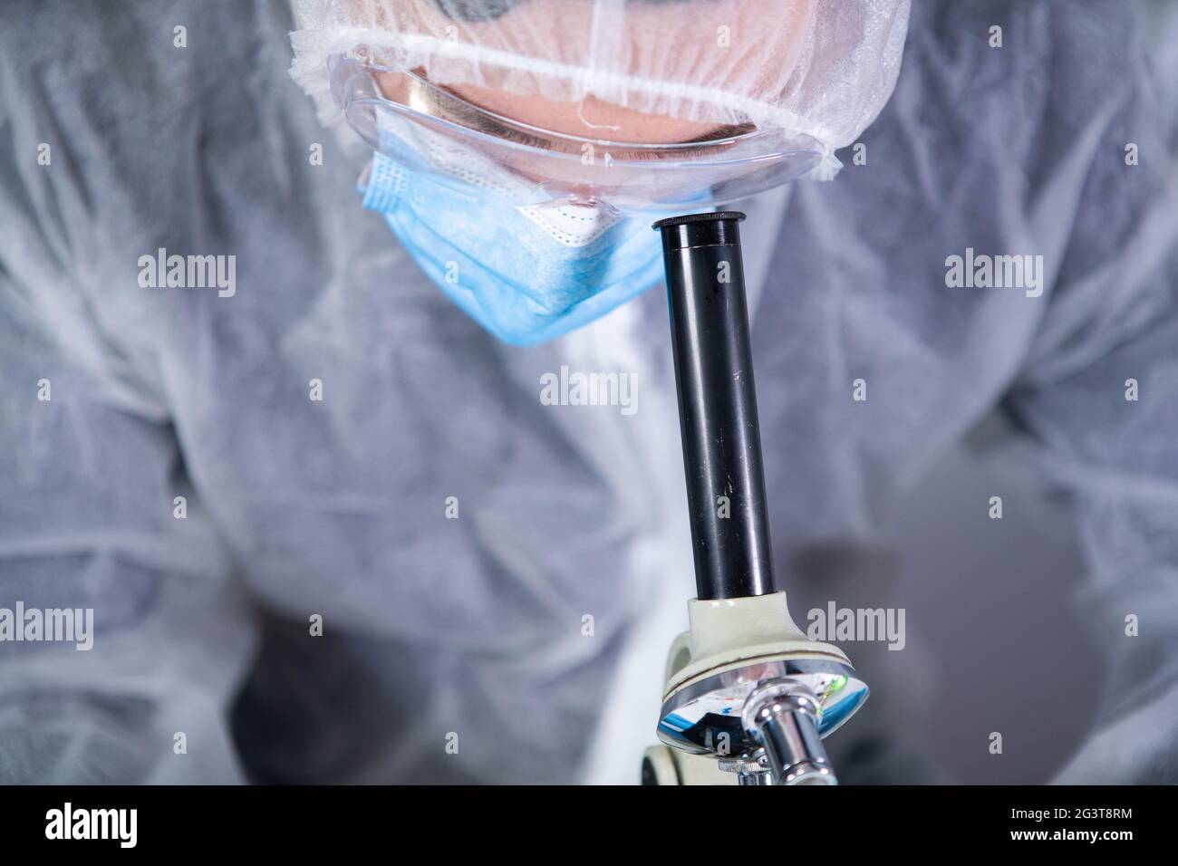 Professionnel de la santé en costume de protection blanc regardant à travers le microscope en laboratoire chimique. Rechercher le coronavirus du vaccin. COV Banque D'Images