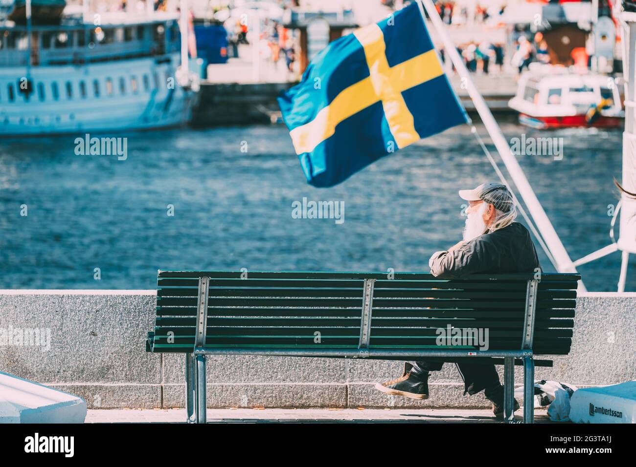 Stockholm, Suède. Old Man se trouve sur un banc près de la City Promenade. En arrière-plan UN drapeau suédois agitant. Banque D'Images