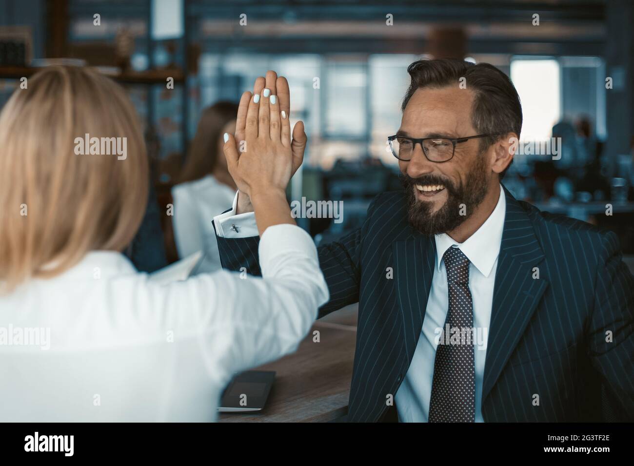 Un travail d'équipe réussi célébrant un homme d'affaires joyeux dans des lunettes donnant cinq hauts avec une femme de collègue debout à l'avant Banque D'Images