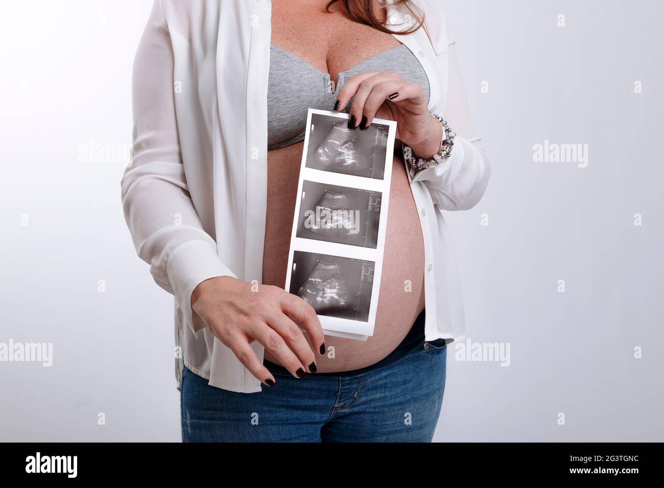Femme enceinte méconnue tenant des images échographiques de son bébé à naître sur le ventre sur fond blanc Banque D'Images