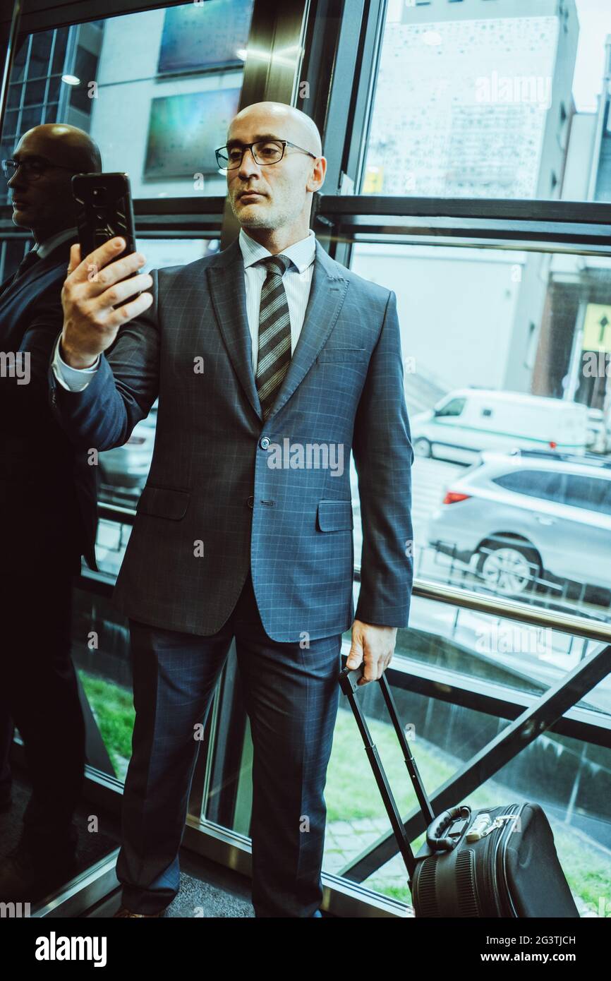Un homme d'affaires en costume peut lire des informations sur le smartphone. L'homme tient son téléphone portable devant lui tout en se tenant à côté Banque D'Images
