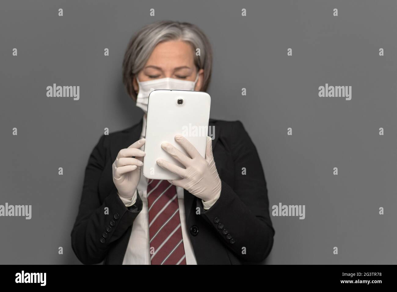Femme d'affaires caucasienne dans le travail de masque de protection sur tablette numérique isolée sur fond gris. Accent sélectif sur le gad électronique Banque D'Images