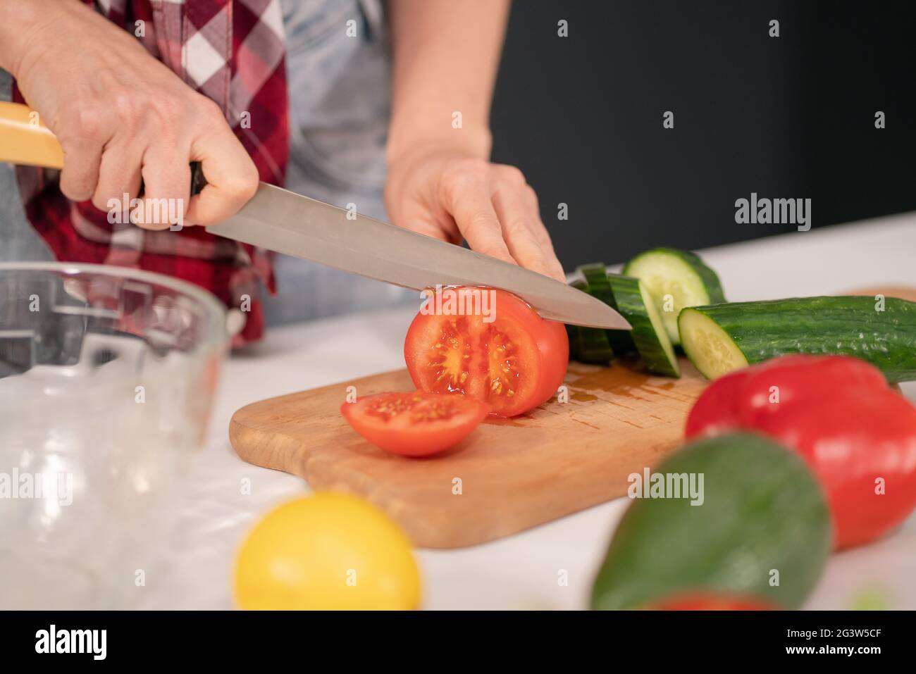 Gros plan. Femme coupant des tomates et des concombres à bord préparant une salade de légumes pour un dîner en famille dans la cuisine. Hé Banque D'Images