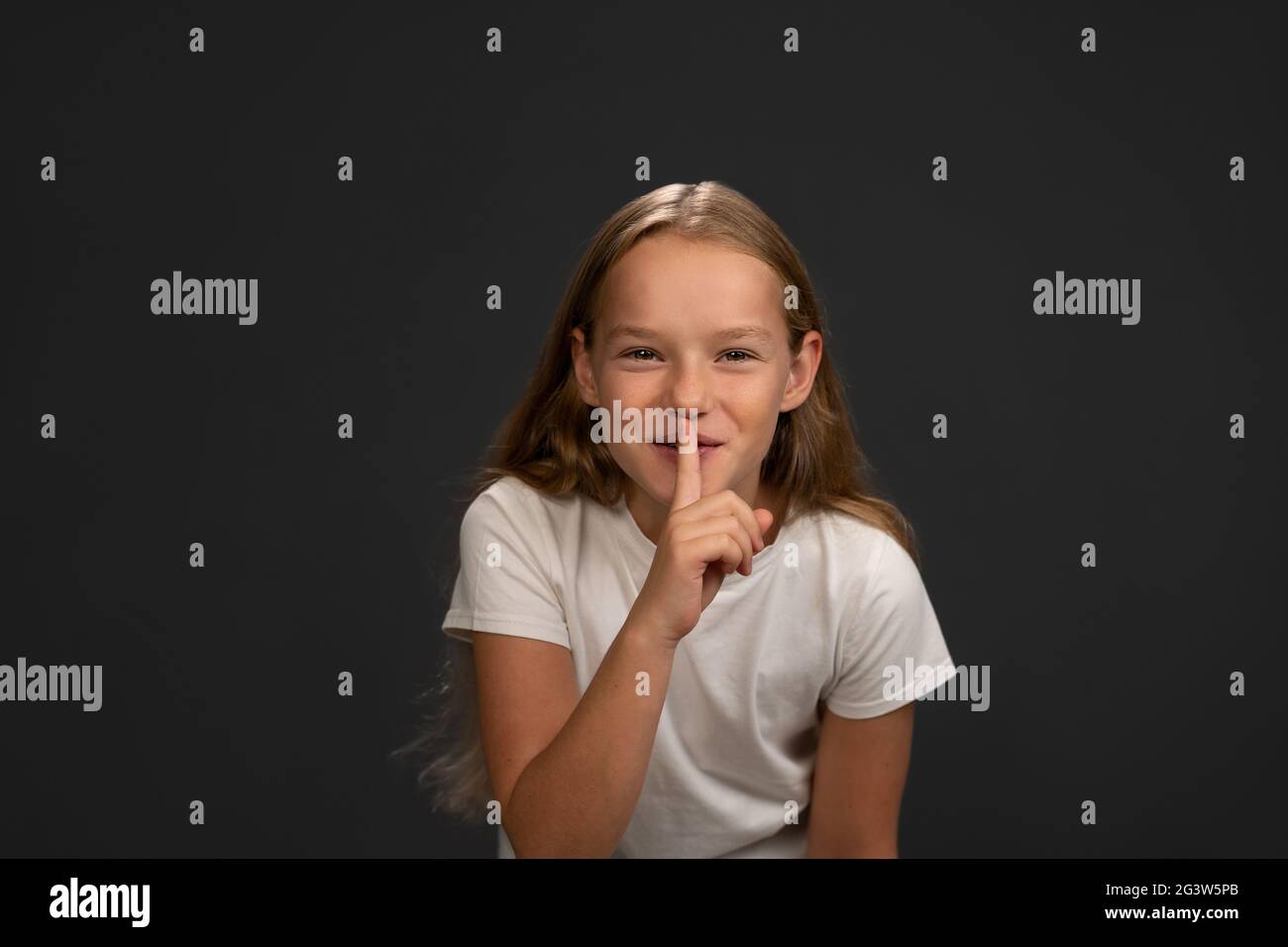 Dire de garder le silence petite fille tient son doigt sur ses lèvres en disant tout le monde. Enfant portant un t-shirt blanc souriant à la came Banque D'Images