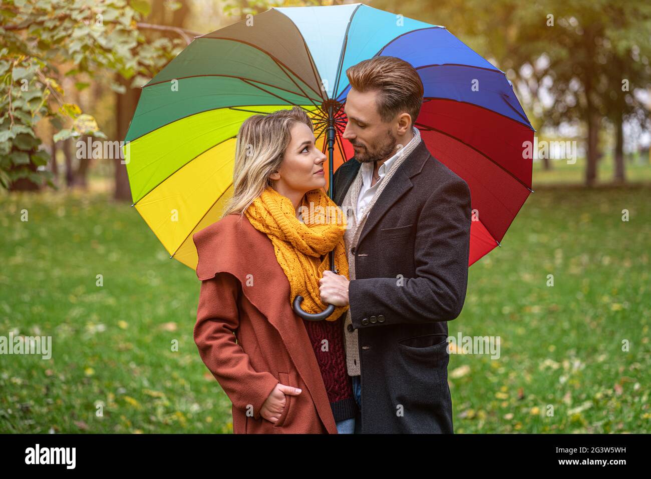 Beau couple amoureux debout dans le parc sous un parapluie de couleur  arc-en-ciel regardant les autres yeux. Une belle fille wal Photo Stock -  Alamy