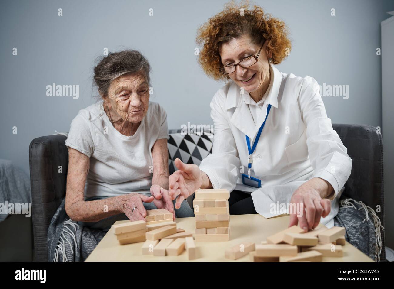 Femme senior pratique des compétences, construire des blocs de bois, construire la tour et essayer de ne pas laisser tomber, jeu Jenga. Bloc d'extraction de l'ancien patient Banque D'Images