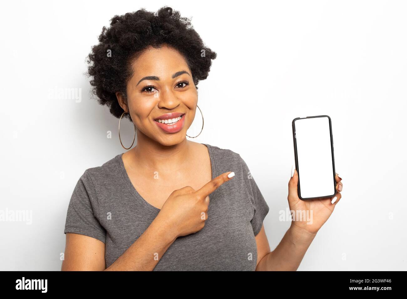 Une femme africaine montre son doigt sur l'écran blanc du smartphone. Une femelle noire tient un téléphone portable. Banque D'Images