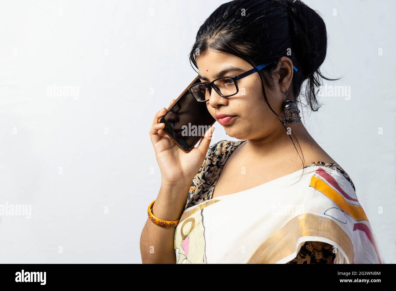 Une belle femme indienne en saree parlant sur un téléphone intelligent avec un visage sérieux isolé sur fond blanc Banque D'Images