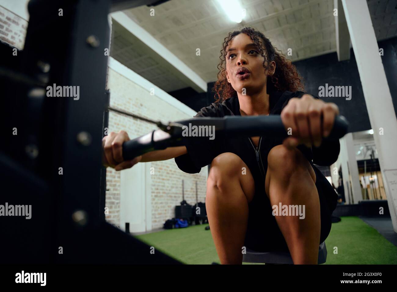 Femme afro-américaine utilisant une machine à ramer pendant l'entraînement en cross-fit. Une athlète féminine s'entraînant intensément dans la salle de sport. Photo de haute qualité Banque D'Images