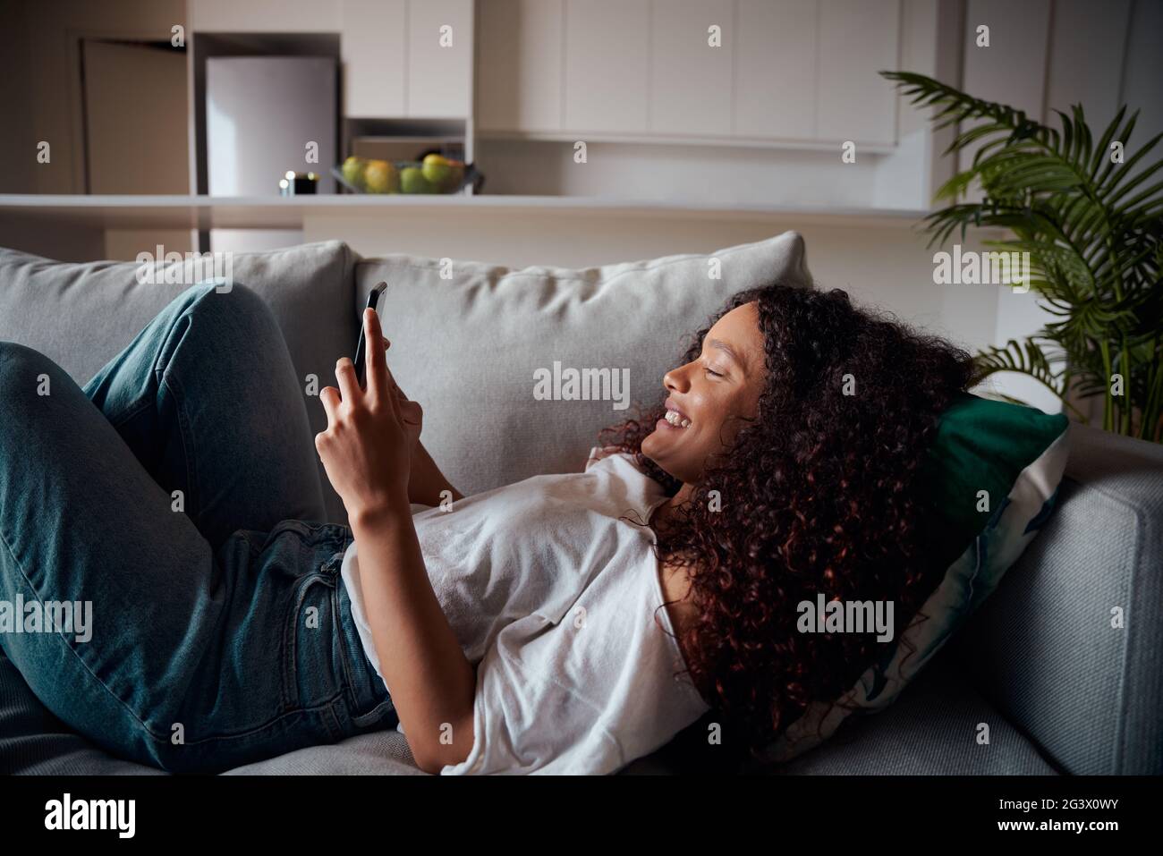 Femelle de race mixte adolescent couché sur le canapé texting sur un appareil cellulaire Banque D'Images