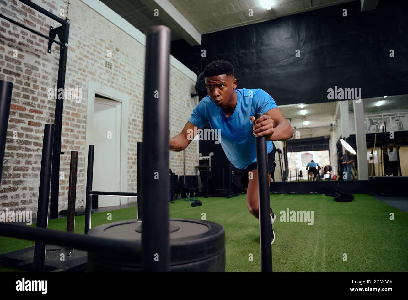 Afro-américain qui s'entraîne intensément lors d'une formation croisée. Athlète masculin poussant le traîneau dans la salle de gym. Photo de haute qualité Banque D'Images
