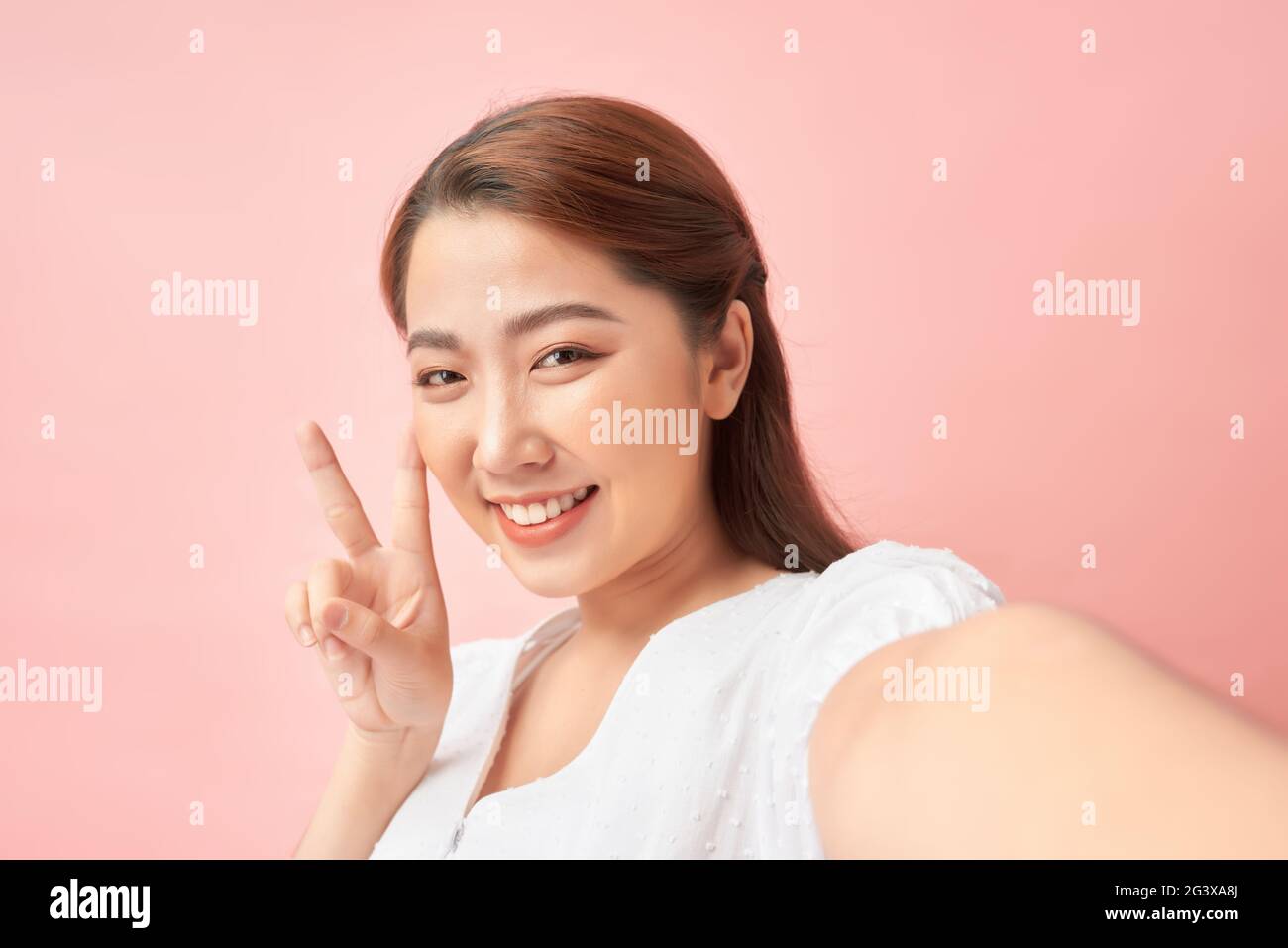 Jeune femme gaie prenant un autoportrait et gestante V-signe sur fond rose Banque D'Images
