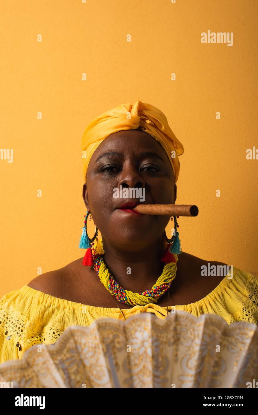 portrait d'une femme afro-américaine sérieuse d'âge moyen fumant un cigare sur du jaune Banque D'Images