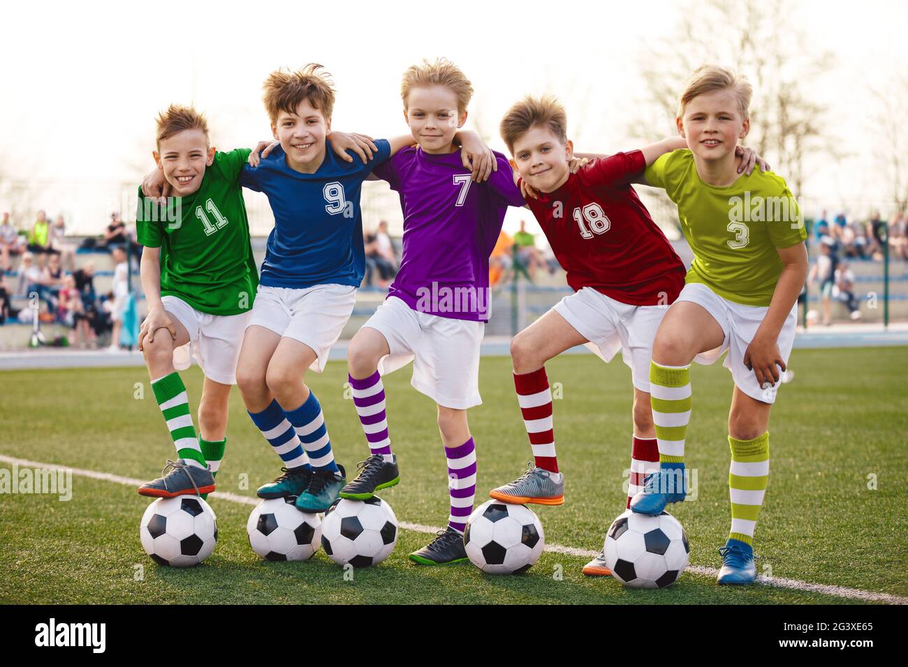 Groupe de jeunes garçons de football heureux en uniforme de jersey coloré. Cinq enfants joyeux avec des ballons de football souriant regardant la caméra. Enfants dans Banque D'Images