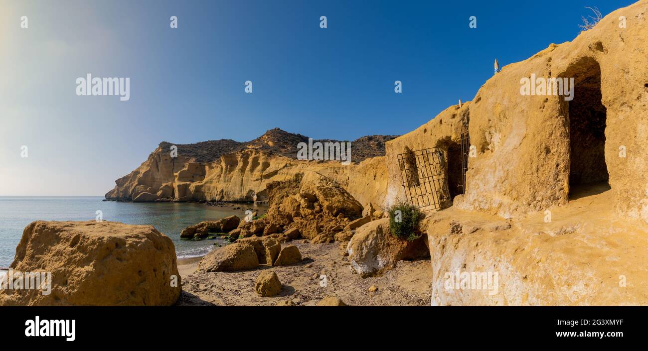 Vue sur les grottes et les habitations en grès avec les falaises derrière à Une crique idyllique et une plage sur la côte de Murcia Banque D'Images