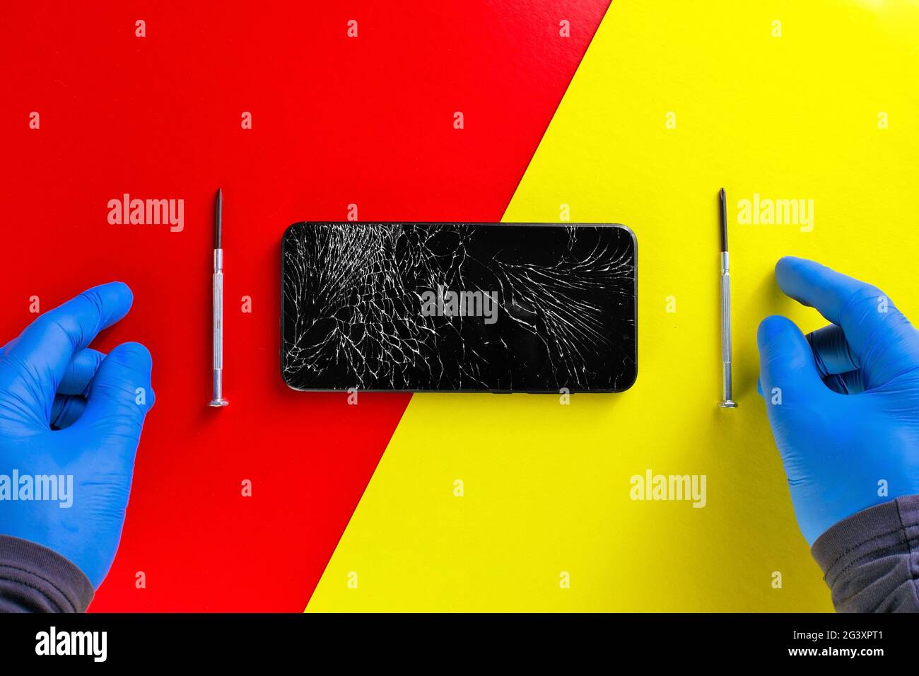 Les mains gantées d'un réparateur de matériel à côté de tournevis et d'un téléphone cassé sur fond jaune-rouge. Vue de dessus Banque D'Images