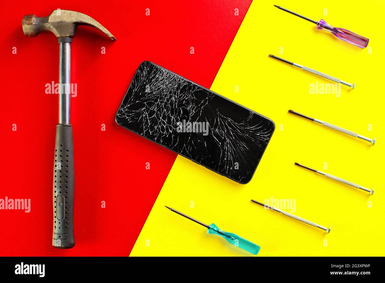 Un téléphone noir à écran tactile avec un écran fissuré à côté des tournevis et un marteau sur un fond coloré et lumineux. Banque D'Images