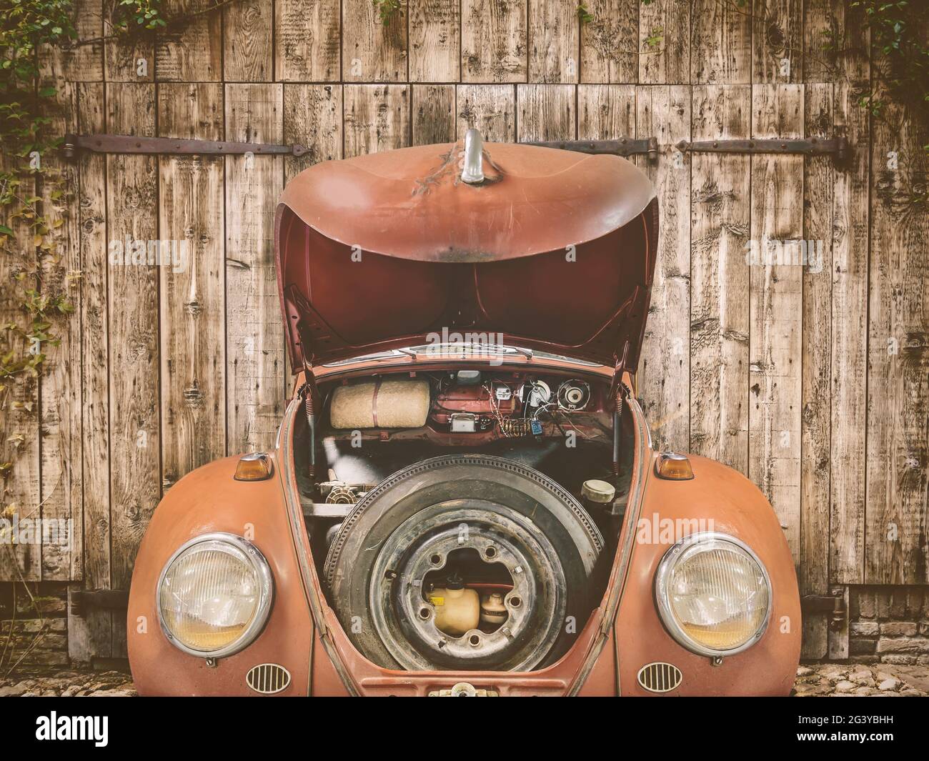 Voiture classique rouge rouillée avec capot ouvert devant une ancienne porte de grange Banque D'Images