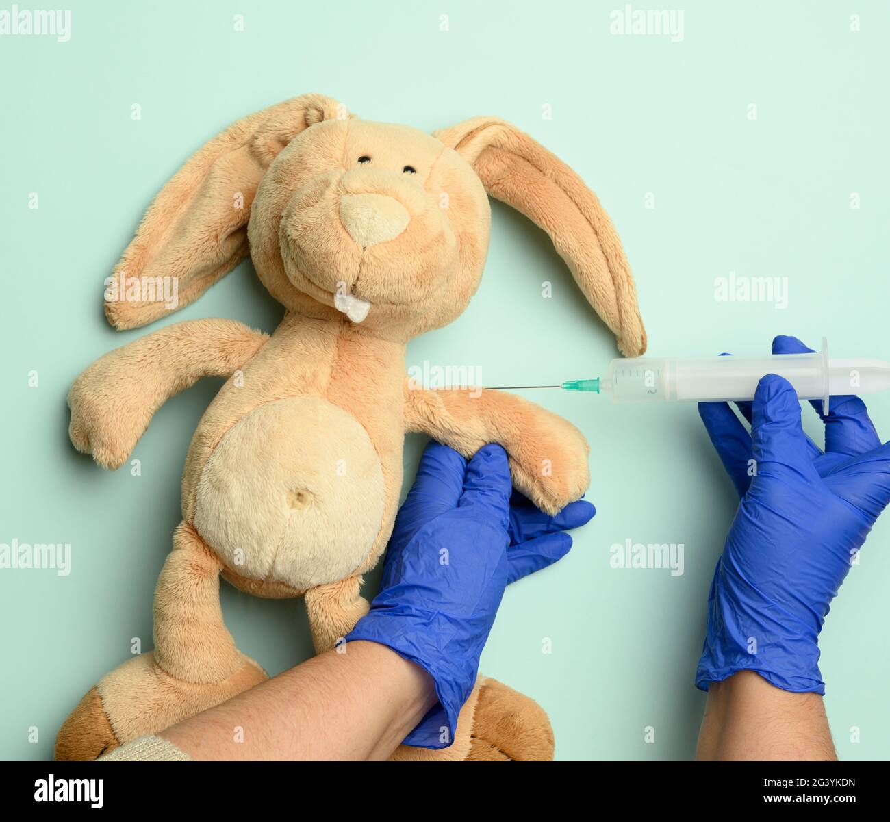Lapin en peluche et deux mains femelles d'un médecin injectant une injection sur fond bleu Banque D'Images