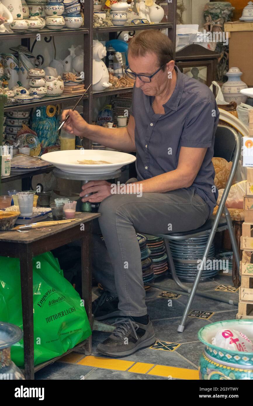 Un atelier d'artisanat à Vietri - Italie. Un artisan peint une plaque d'argile. Souvenirs faits main. De nombreux objets de poterie sur les étagères d'exposition. Banque D'Images