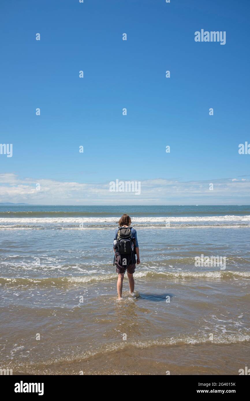Femme marchant dans des vagues peu profondes sur une plage de sable. Banque D'Images