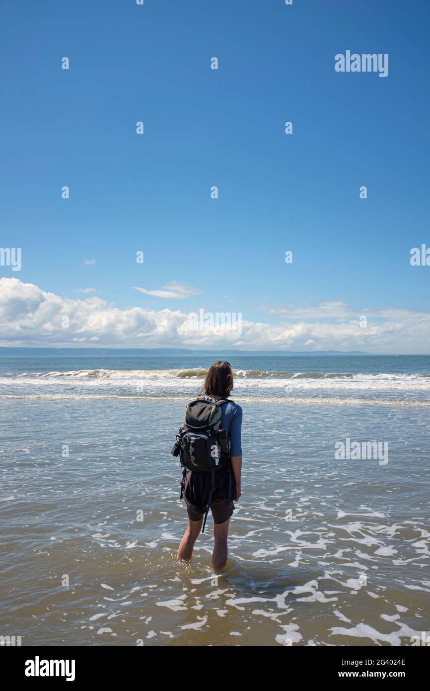 Femme marchant dans des vagues peu profondes sur une plage de sable. Banque D'Images