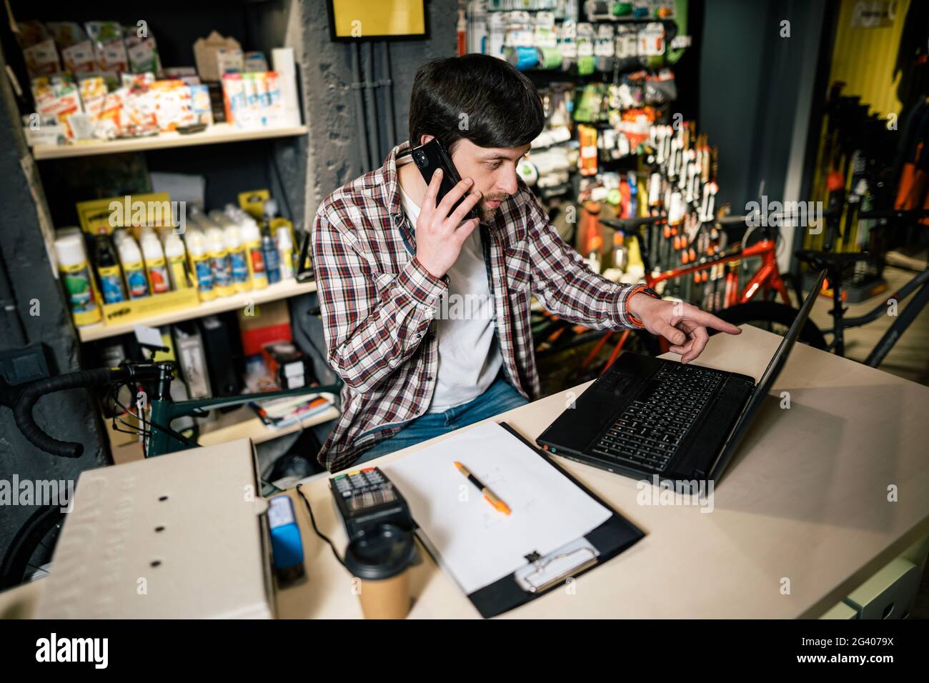 Propriétaire d'une petite entreprise au téléphone et à l'ordinateur dans le magasin. Un travailleur de la boutique de sport fait un appel avec un téléphone cellulaire. Vendeur travaillant et parlant Banque D'Images