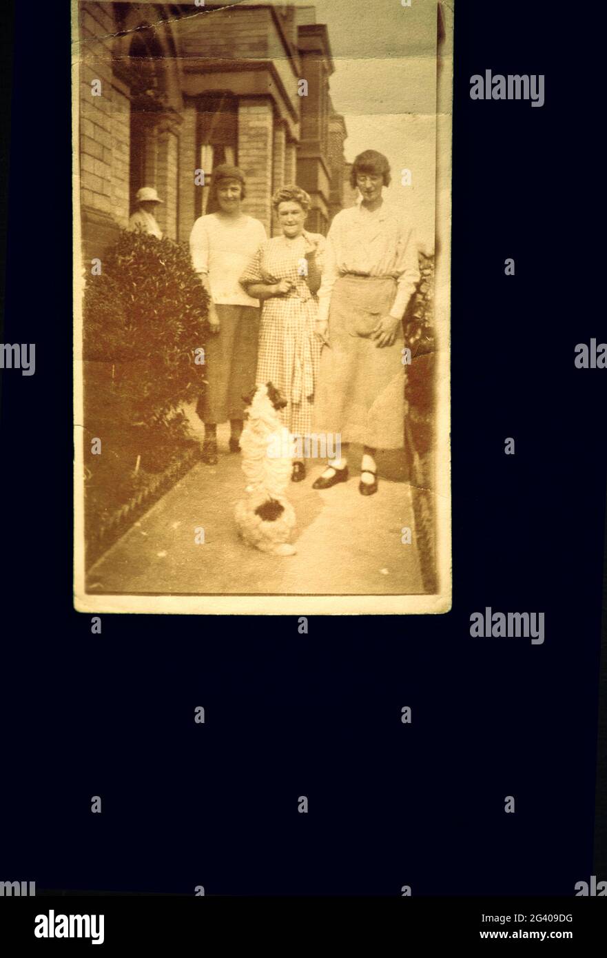 1910 authentique photographie vintage de deux jeunes femmes une femme et un chien adulte de taille moyenne debout à l'extérieur de la maison. Concept de nostalgie, famille, historique Banque D'Images