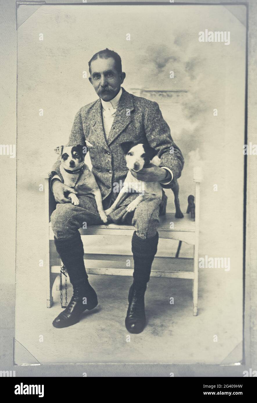 Photographie vintage authentique d'un homme adulte senior assis sur une chaise tenant deux chiens. Concept de la convivialité, de l'amitié, meilleur ami des ans Banque D'Images