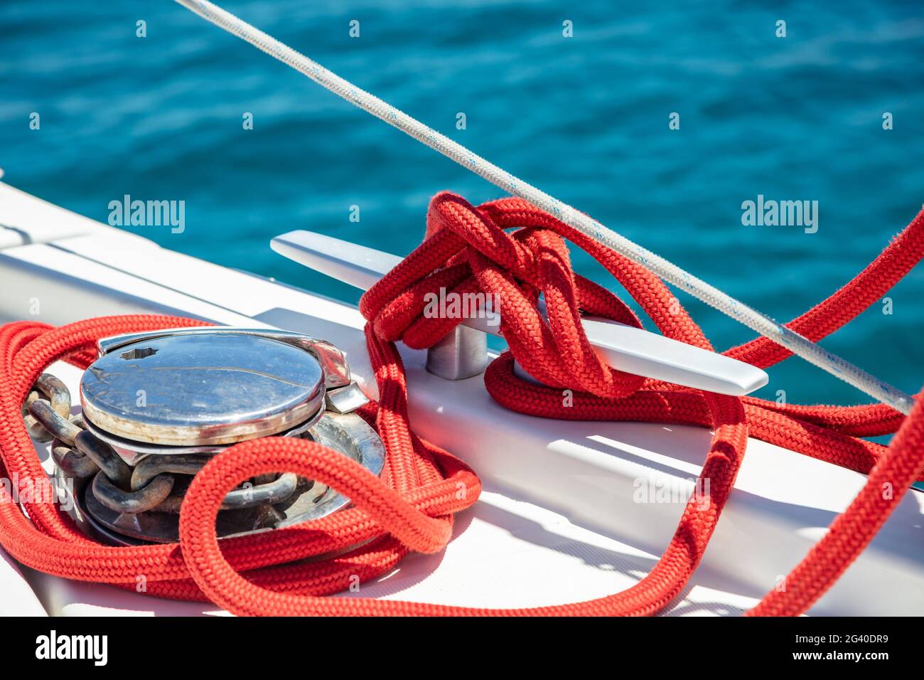 Bateau à voile amarrer des cordes sur le pont. Corde de yachting de couleur rouge attachée sur la cale. Chaîne métallique lourde autour du treuil, espace, gabarit de carte de croisière. Sailbo Banque D'Images