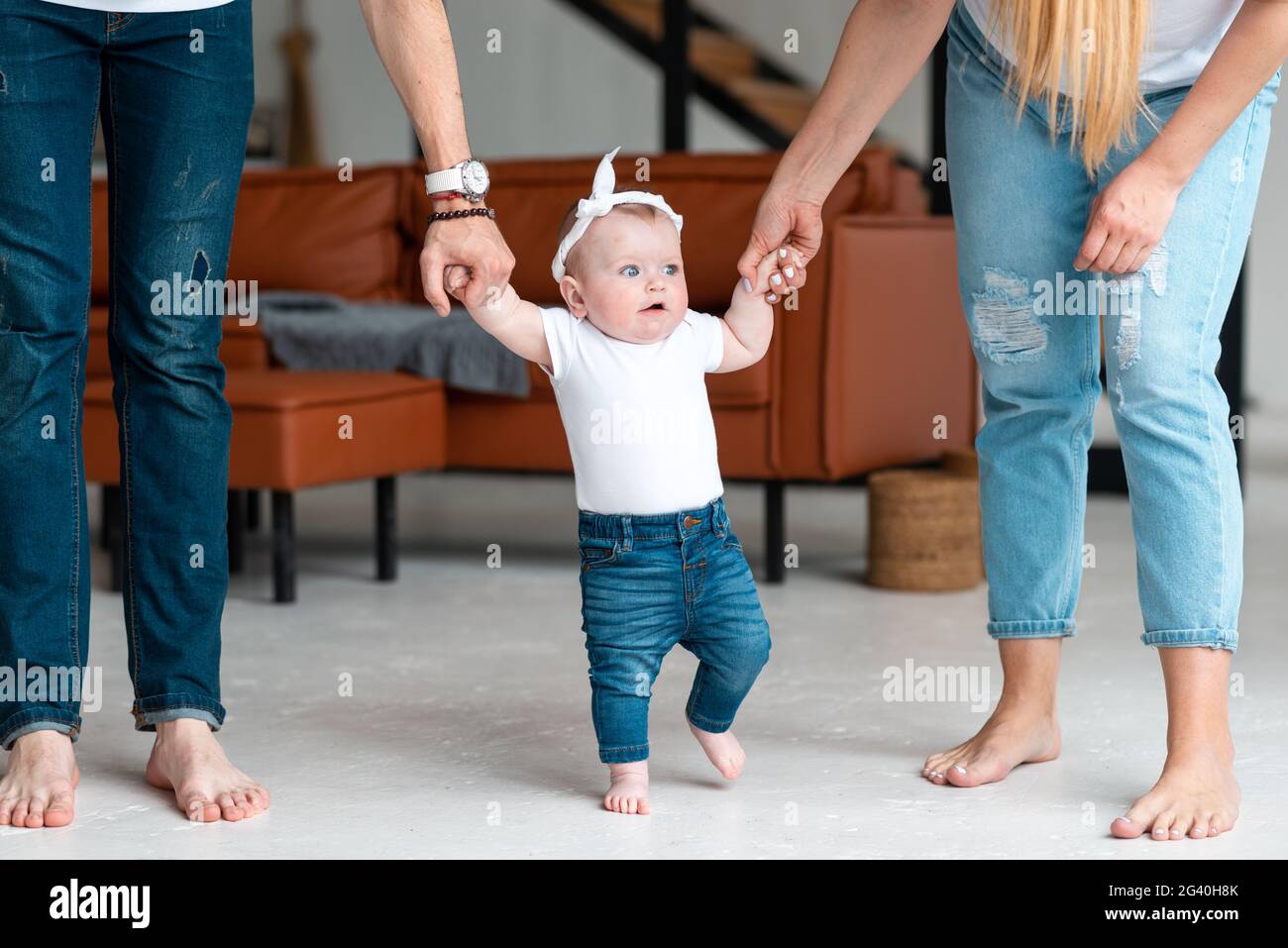 Les parents tiennent une petite fille mignonne par les poignées, lui apprennent à marcher Banque D'Images