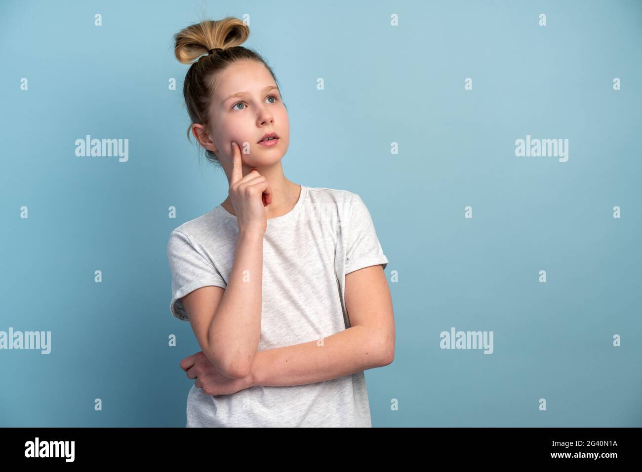 Conçu une adolescente dans un T-shirt blanc sur fond bleu. Jolie petite fille isolée sur fond de mur vierge. Banque D'Images