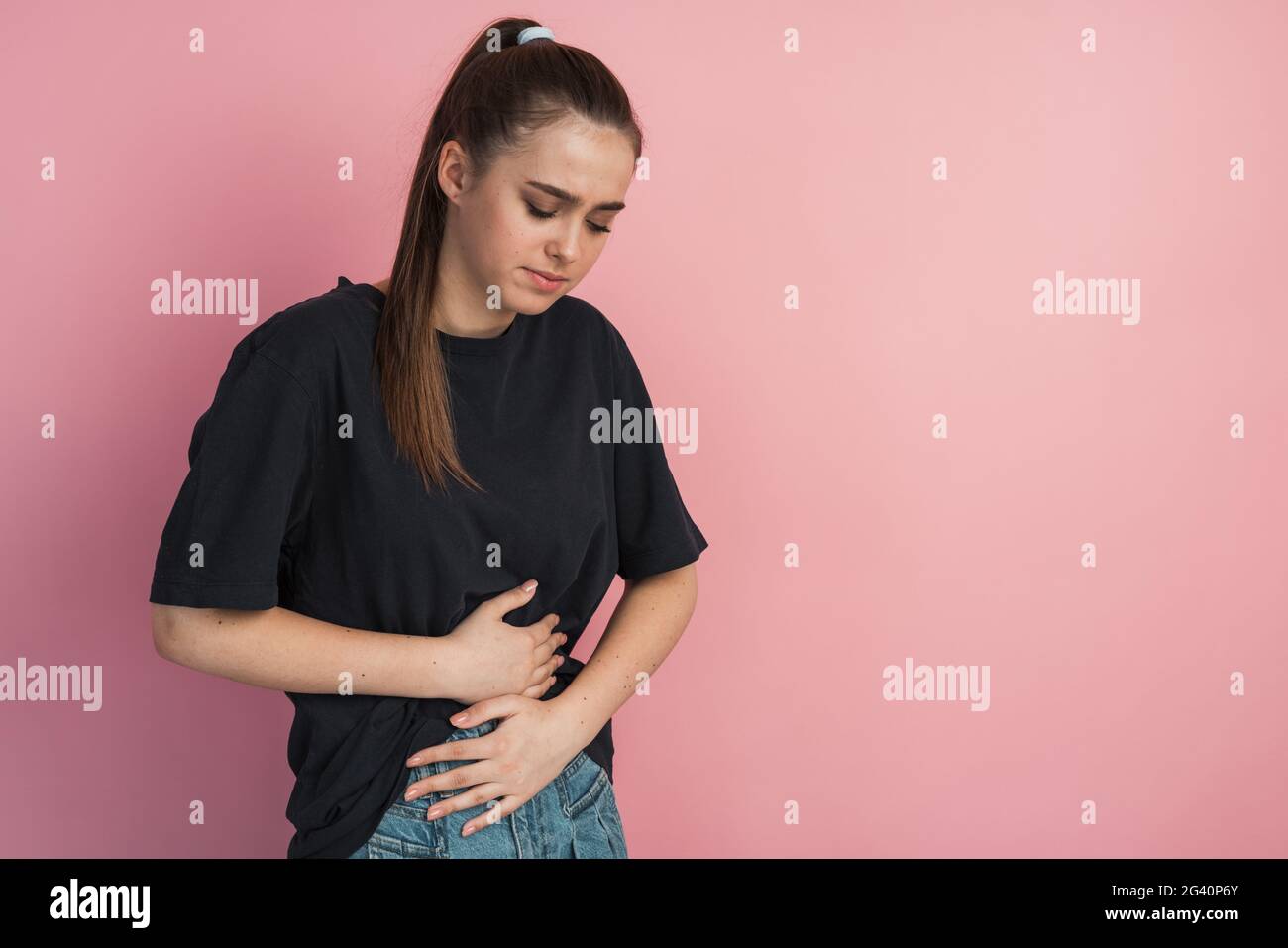 La pauvre fille a attrapé son estomac sur un fond rose isolé. Elle se vante dans la douleur., pauvre fille attrapa son estomac sur un fond rose isolé. Elle Banque D'Images