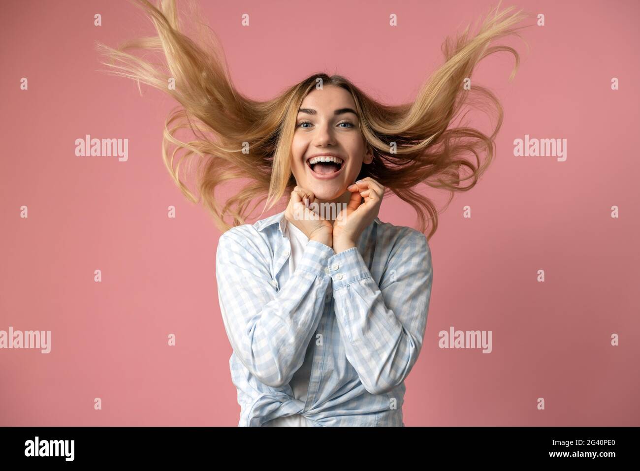 Blonde naughty jette ses cheveux, il vole dans l'air. Fille ludique sur fond de mur rose. Banque D'Images