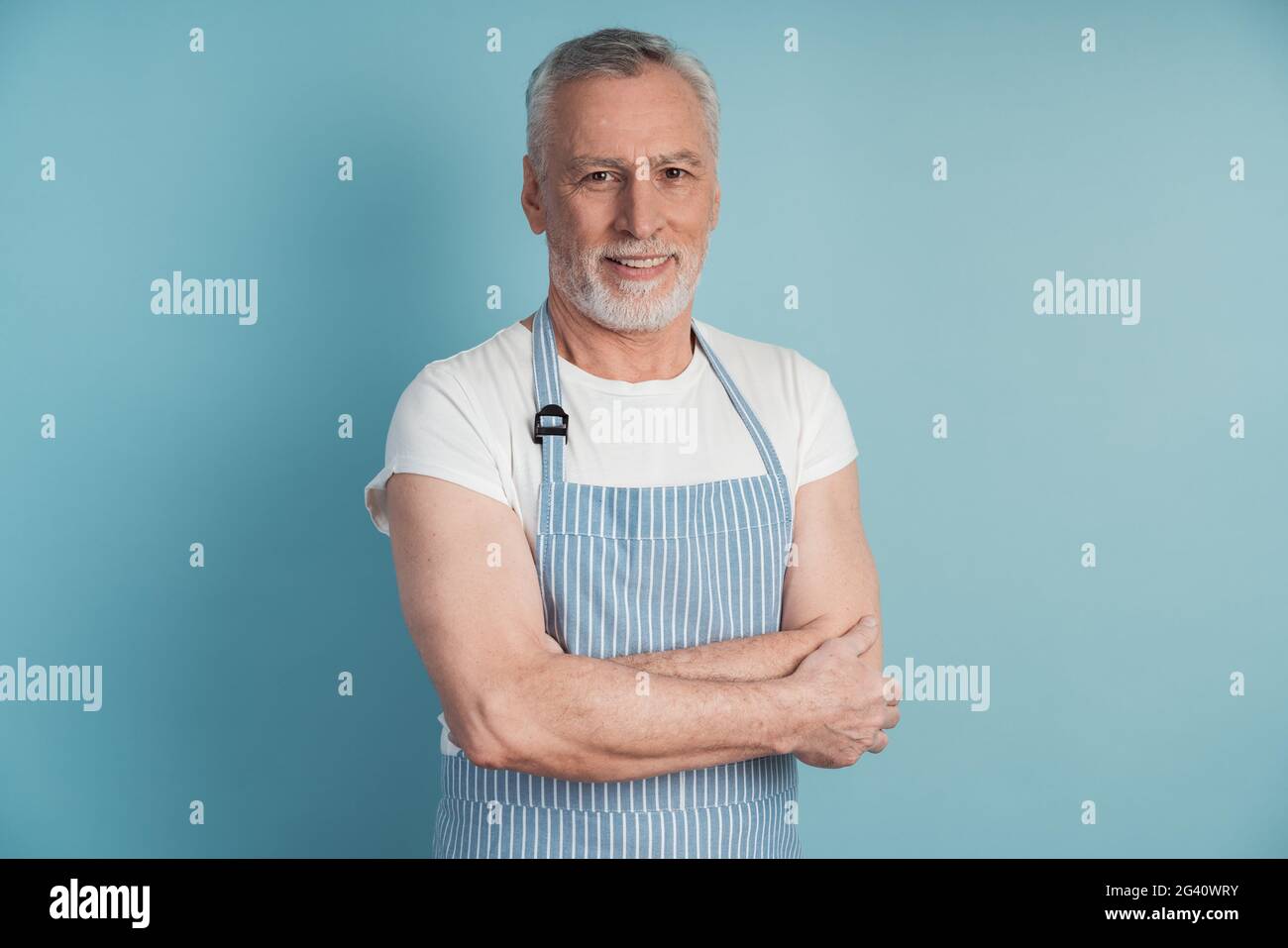 Beau, homme âgé dans un tablier bleu posant sur un fond bleu. Beau homme isolé sur fond de mur vierge Banque D'Images