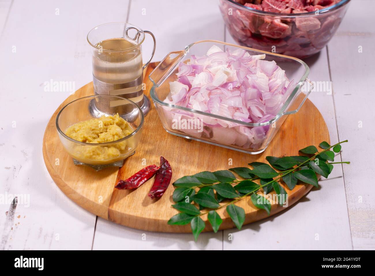 Ingrédients - oignon haché, pâte d'ail au gingembre, feuilles de curry, huile de cuisson et piment sec disposés sur une base en bois avec fond texturé. Banque D'Images