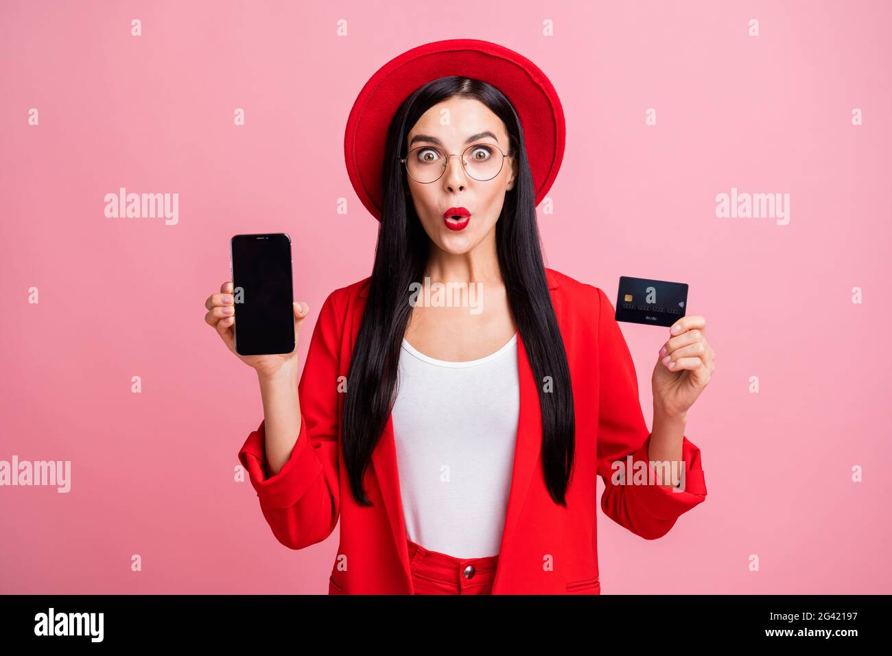 Photo portrait de fille stupéfait tenant téléphone de carte de crédit avec espace vide dans les mains isolées sur fond rose pastel Banque D'Images