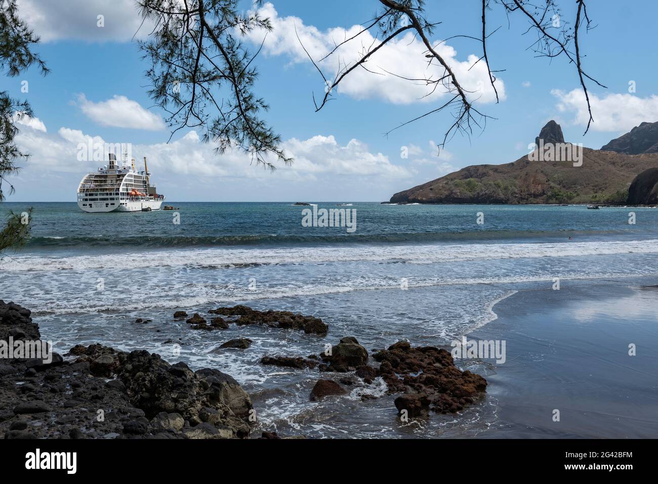 Rochers sur plage de sable noir avec le cargo de passagers Aranui 5 (Aranui Cruises) amarré dans la baie, Puamau, Hiva OA, îles Marquesas, Polynésie française, Sou Banque D'Images