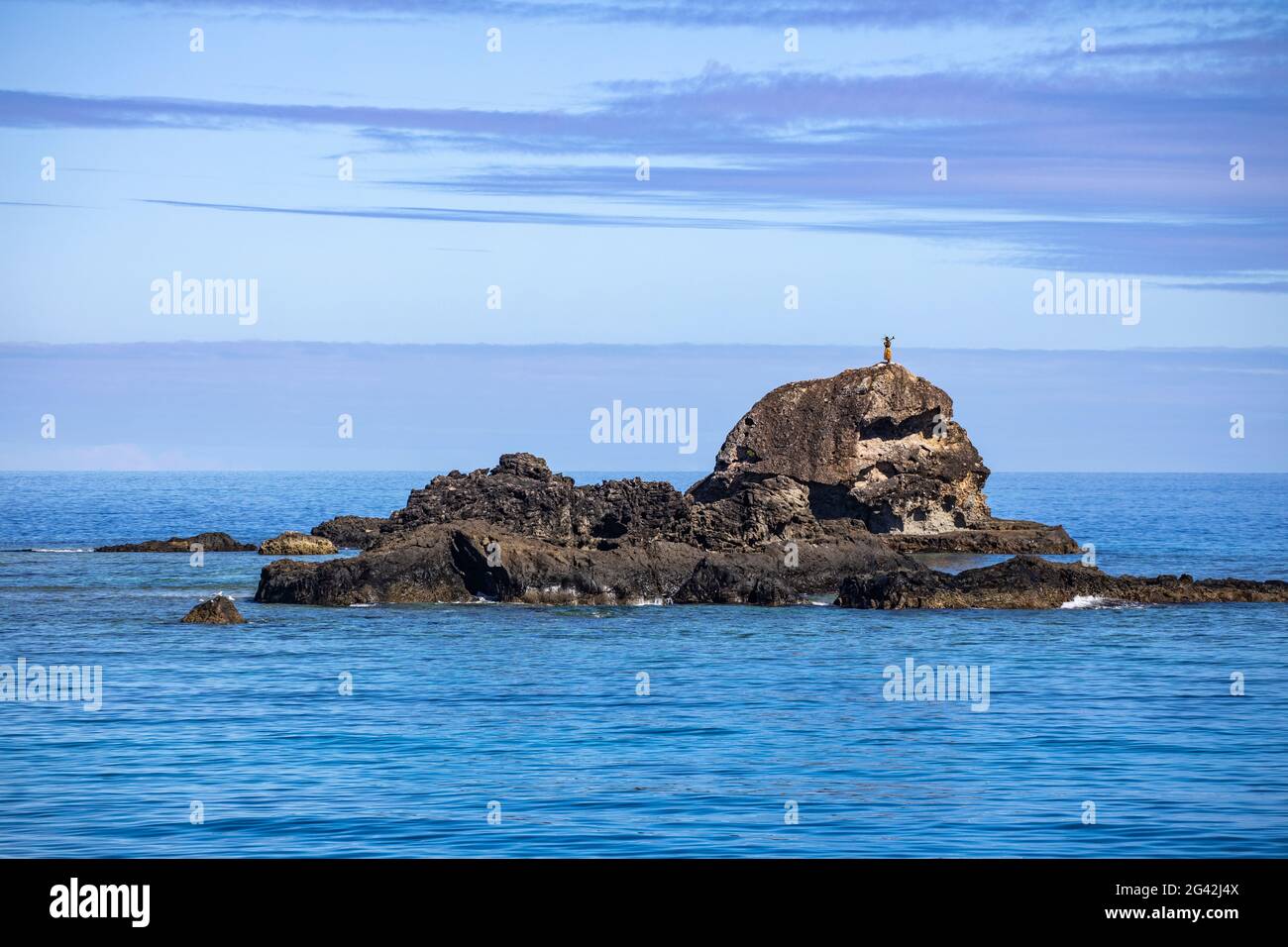Un Fijian se dresse sur un rocher et accueille les passagers sur le catamaran Yasawa Flyer II (South Sea Cruises) à l'approche du tra de l'archipel de Yasawa Banque D'Images