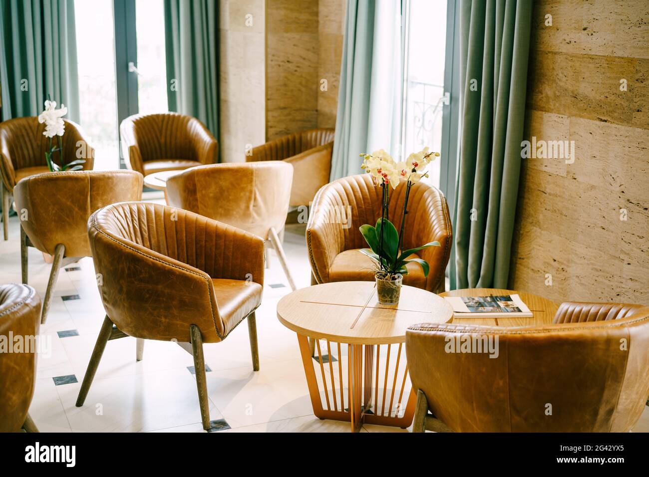 Un grand hall avec des sorties sur le balcon avec des tables rondes et des fleurs et des fauteuils bruns en cuir véritable. Banque D'Images