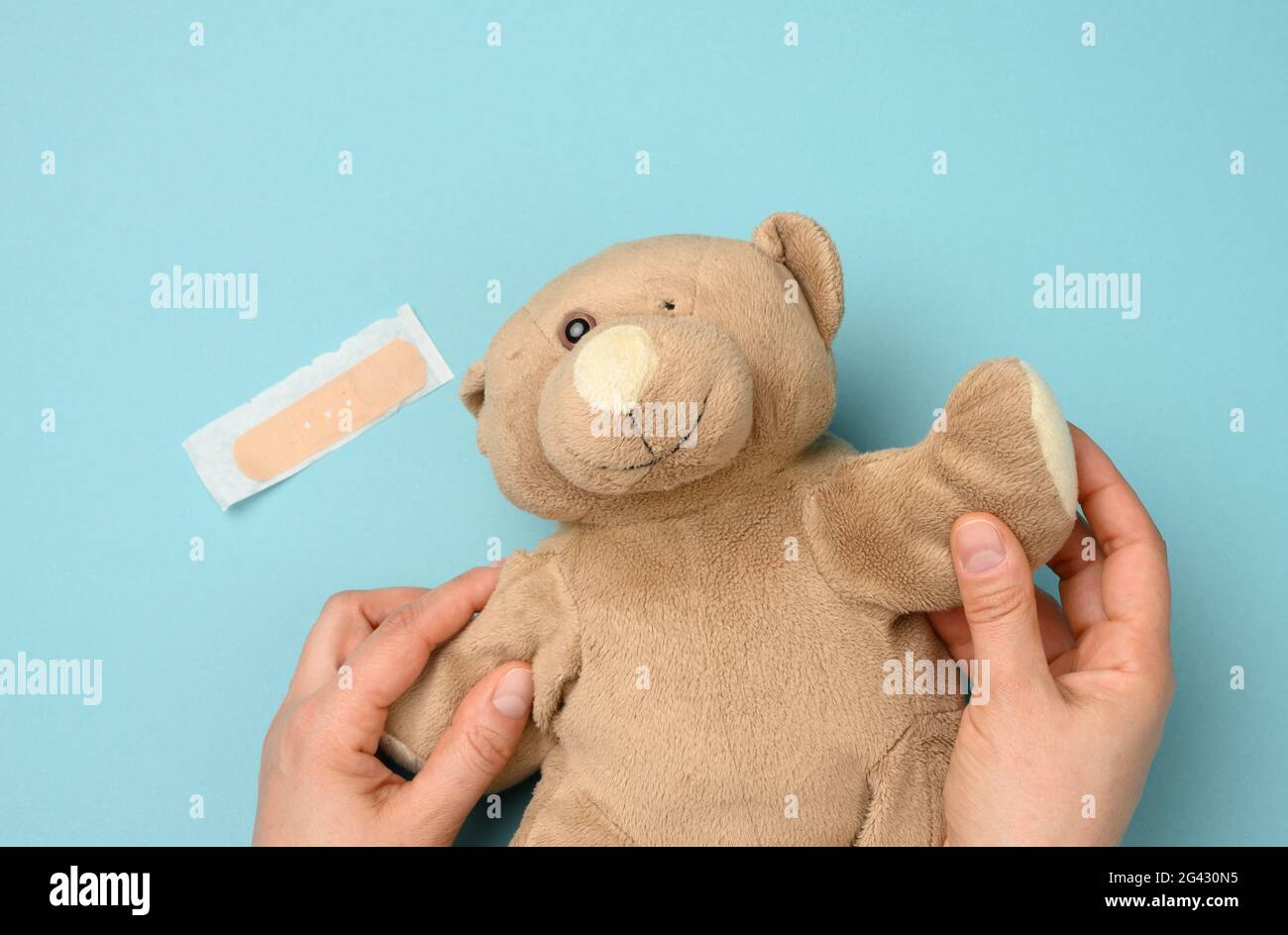 Main féminine tenant un ours en peluche brun avec un œil déchiré sur un  fond bleu Photo Stock - Alamy