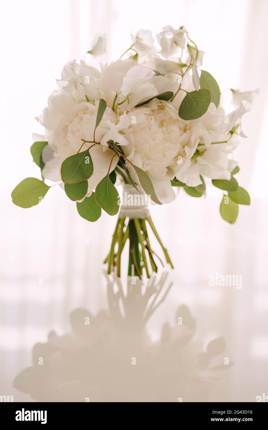 Bouquet de mariée de pivoines blanches, pois doux et branches d'eucalyptus sur une table blanche brillante Banque D'Images