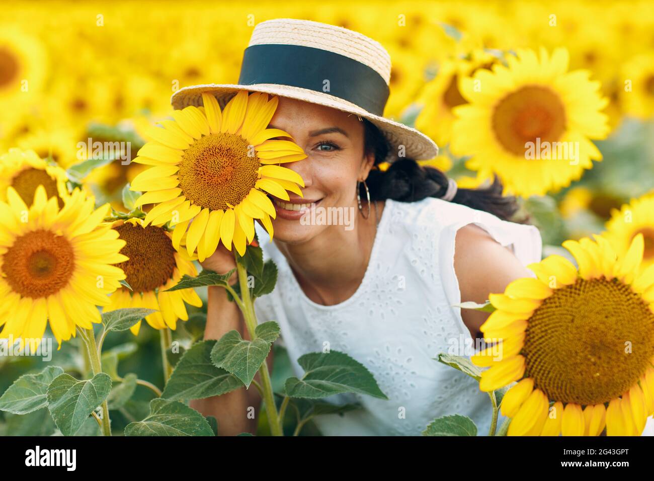 Belle jeune femme souriante dans un chapeau avec fleur sur son œil et son visage sur un champ de tournesols Banque D'Images
